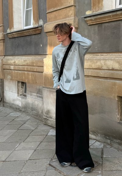 Camisa de manga larga azul claro con un estampado gráfico, combinada con pantalones anchos negros y zapatillas grises, en un entorno urbano.