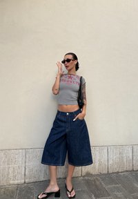 Raidallinen harmaa lyhyt paita punaisella graafisella printillä, avarat tummansiniset culottes-housut, mustat slingback-sandaalit, musta käsilaukku ja ovaalit aurinkolasit.