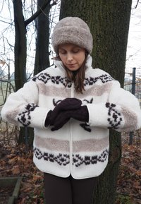 Bela jopica iz flisa z bež in rjavimi vodoravnimi črtami, vzorčaste poudarke ter sprednjo zadrgo. Rjave pletene rokavice in ujemajoča kapa.