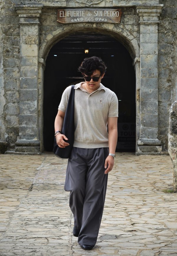 Jeune homme portant des lunettes de soleil et un sac, marchant sur un chemin de pierre devant l'entrée de la forteresse El Fuerte de San Pedro.