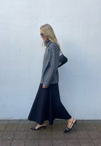 Pelēka adīta rolka, plūstoša melna svārku kleita un melnas augstpapēžu slingback kurpes. Sieviete nēsā mazu melnu rokassomu.