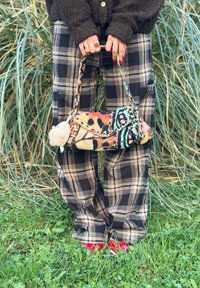 Fargerik mønstrete clutch-veske med kjedehank, med livlige motiver i rødt, grønt og gult; fluffy aksent festet. Brukt med rutete bukser.