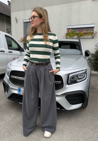 Top de rayas verdes y blancas de canalé, pantalones anchos grises con pliegues, cinturón de cuero marrón, combinado con zapatillas blancas. Coche de fondo.