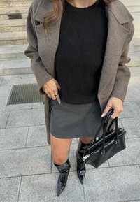 Smeđi kaput, crni pulover, sivi rebrasti suknja, crne lakirane čizme do koljena s šiljastim nožnim prstima te mala crna torbica.
