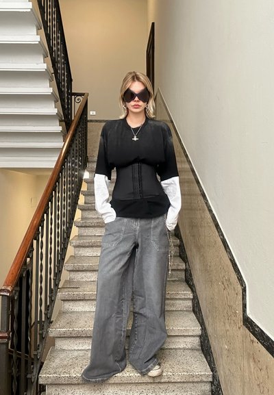 Top oversized en blanco y negro con una cintura ajustada, combinado con pantalones anchos grises. Gafas de sol negras elegantes y un collar de plata completan el look.