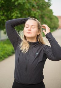 Zwarte sportieve zip-up top gemaakt van lichtgewicht stof, met lange mouwen en een klein logo op de borst, gedragen met zwarte broek.