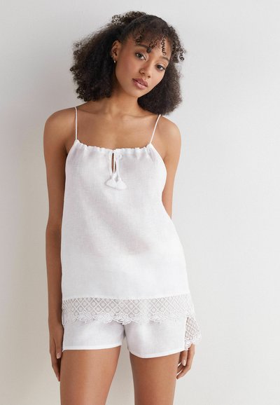 Camiseta sin mangas de lino blanco con delicado escote con volantes y detalle de ojal, acompañada de pantalones cortos a juego con bordado de encaje en el dobladillo.