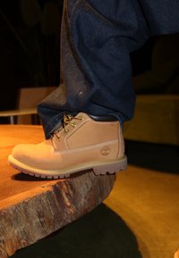 Καφέ δερμάτινο μποτάκι μέχρι τον αστράγαλο με γκρι λεπτομέρειες, κίτρινες και κόκκινες κορδόνες, και ανθεκτική σόλα, τοποθετημένο σε ξύλινη επιφάνεια.