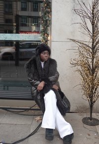 Zwarte donsjas met nep bontkraag, gedragen over een witte coltrui en wijde broek. Zwarte plateau laarzen en een bijpassende bontmuts.