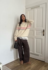 Pull-over blanc cassé avec des rayures roses et grises, assorti à un pantalon ample marron foncé. Accessoire : un petit sac noir. Texture lisse.