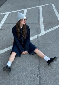 Τζάκετ denim και σορτς σε σκούρο μπλε, γκρι πλεκτό σκουφί, μαύρα παπούτσια, λευκές κάλτσες, καθισμένος σε άσφαλτο με λευκές γραμμές στάθμευσης.