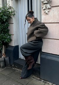 Braune Hahnentritt-Übergroßjacke, graue weite Hose und braune Stiefel mit Absatz. Glatte Texturen, dezente Muster und lockere Passform.