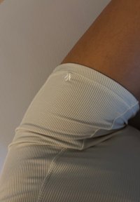 Licht beige, geribbelde leggings met een strakke pasvorm, met een close-up van de elastische tailleband en de huidkleur bij het kniegewricht.