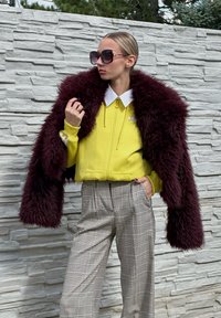 Casaco amarelo com fecho, colarinho branco, combinado com calças largas de xadrez. Um casaco de pelúcia burdeos oversized e óculos de sol grandes completam o visual.