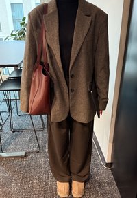 Šedý štruktúrovaný blazer cez čierny rolák, spárovaný s voľnými čiernymi nohavicami, hnedými slip-on topánkami a bordovou koženou kabelkou.
