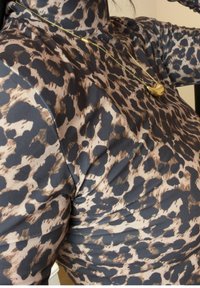 Gros plan sur une personne portant un haut à imprimé léopard et un collier en or avec un pendentif de forme irrégulière.