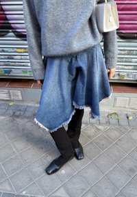 Denim asymmetrical skirt with frayed edges, paired with black trousers and flat shoes. Grey knit jumper and a small light grey bag are also visible.