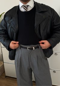 Μαύρο δερμάτινο μπουφάν μοτοσικλέτας πάνω από ένα�ν μαύρο πουλόβερ, συνδυασμένο με γκρι πλισέ παντελόνι και μια μαύρη ζώνη με ασημί κούμπωμα.