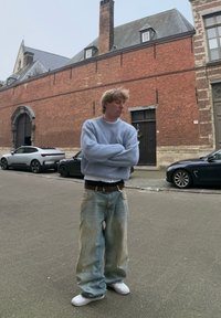 Ανοιχτό μπλε πλεκτό πουλόβερ, oversized και υφασμένος, συνδυασμένο με χαλαρά τζιν που έχουν ξεθωριασμένες άκρες. Λευκά αθλητικά παπούτσια ολοκληρώνουν την εμφάνιση.