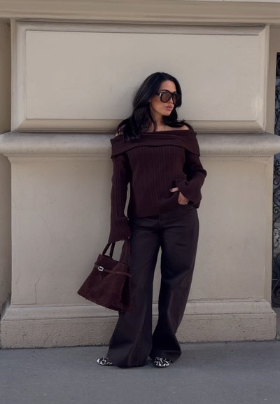Suéter marrón de canalé con escote off-the-shoulder y mangas largas, combinado con pantalones marrones de pierna ancha y un bolso de ante marrón.
