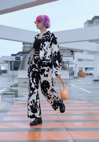 Sort og hvid cow-print jakke og matchende brede bukser. Sort top, orange håndtaske og sorte platform sko. Klare oversized solbriller.