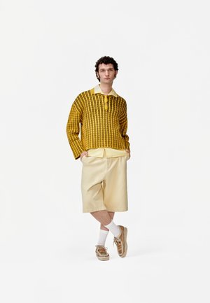 Suéter de punto amarillo con rayas verticales negras, pantalones cortos beige y zapatillas de deporte con estampado. Mezcla de algodón; cierre de botón en el cuello.