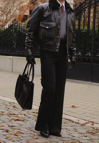 Czarna skórzana kurtka typu bomber z futrzanym kołnierzem, szary sweter, czarne spodnie o szerokich nogawkach, czarne rękawiczki i czarna torba typu tote.