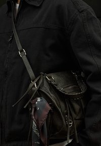 Čierna kožená crossbody taška so zapletenými detailmi, viacerými zipsovými priehradkami a pripojenou šatkou s motívom.