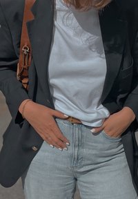 Μαύρο σ�ακάκι πάνω από λευκή μπλούζα, συνδυασμένο με ανοιχτό μπλε ψηλόμεσες τζιν παντελόνες. Καφέ ζώνη, χέρια στη μέση, επιδεικνύοντας ένα βραχιόλι και ένα δαχτυλίδι.