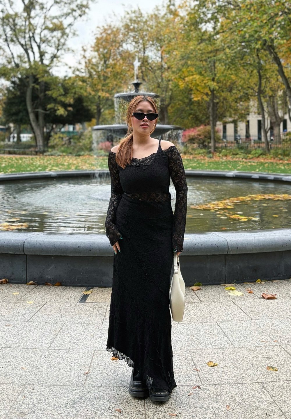 Robe noire en dentelle à manches longues avec un design décolleté, texture superposée et ourlet festonné, assortie à des bottes à plateforme noires et un sac léger.