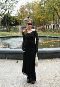 Robe noire en dentelle à manches longues avec un design décolleté, texture superposée et ourlet festonné, assortie à des bottes à plateforme noires et un sac léger.