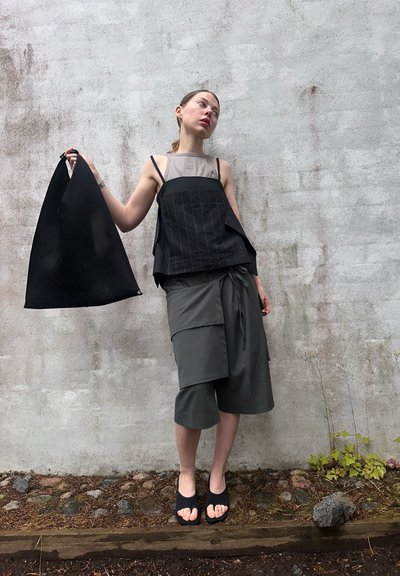 Top de rayas negras con diseño asimétrico, pantalones cortos grises de corte holgado y una bolsa tote negra. El conjunto presenta diversas texturas y siluetas.