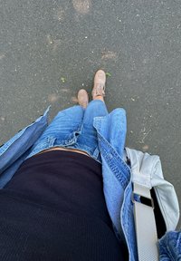En jeansjakke, svart ribbestrikket tanktopp, blå shorts og beige joggesko. En veske med en grå stropp ligger ved siden av. Bakken er mørk med spredte blader.