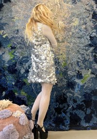 Robe à sequins argentée sans manches, assortie à des collants blancs texturés et des talons compensés noirs, sur un fond abstrait bleu.