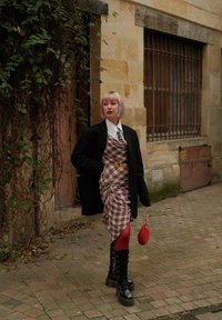 Sort oversized blazer, ternetkjole med ruching, røde strømpebukser, robuste sorte støvler og en lille rød håndtaske. Struktureret brostensbelagt gade.