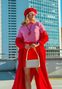 Červený trenčkot přes růžový top, doplněný červenou mini sukní. Doplňky zahrnují červenou baretu, sluneční brýle a malou b�ílou kabelku.