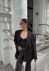 Zwarte pinstripe oversized blazer over een donkere body met kantafwerking; gecombineerd met hoge zwarte leren broek en zonnebril.