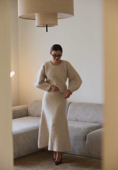 Suéter de punto texturizado en color beige con mangas voluminosas, combinado con una falda larga a juego, en un espacio de vida suave y en tonos neutros.