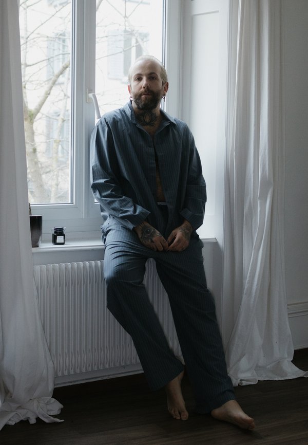 Conjunto de pijama a rayas azules hecho de tela suave, que presenta una camisa y pantalones de corte holgado, con un ajuste relajado. Los pies están descalzos.
