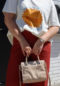 Κρεμ βαμβακερή μπλούζα με γραφικό πορτοκαλί ήλιου, κόκκινα παντελόνια από κα πρέτα και μια μικρή μπεζ τσάντα χειρός με μεταλλικές λεπτομέρειες και υφή.