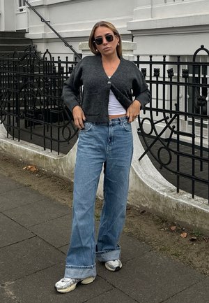 Cárdigan corto gris, top blanco y jeans azul de pierna ancha con puños deshilachados. Combinado con zapatillas plateadas y gafas de sol redondas.