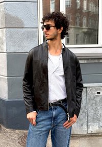 Zwarte leren jas met een staande kraag, met een soepele textuur. Gekozen voor een wit gestreept shirt en blauwe jeans met een gevlochten riem.