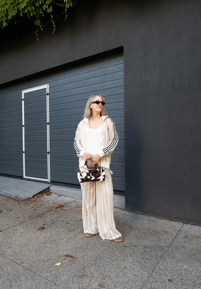 Chándal de malla de color crema con rayas negras, pantalones de pierna ancha a juego y un bolso de mano con un patrón marrón y blanco. Gafas de sol oscuras puestas.