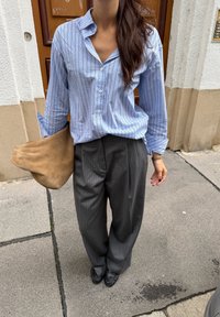 Chemise à rayures bleu clair avec une coupe décontractée, associée à un pantalon ample à rayures grises. Tenant un sac beige doux.