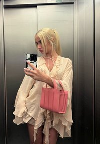 Ljusbeige, rynkad blus med långa ärmar; mjuk rosa, strukturerad handv�äska med vertikal sömnad; elegant, metallisk hissbakgrund.