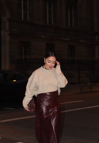 Beige oversized tröja med texturerat tyg, tillsammans med en bourgogne läderkjol. Bär en liten bourgogne väska, med gatubelysning i bakgrunden.