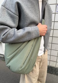 Grüne, gepolsterte Schultertasche mit einem lässigen Design. Trägt man zu hellbeigen Hosen und kombiniert mit einer grauen Zip-Jacke. Glatte Textur.