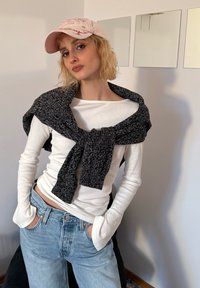 Camicia bianca a maniche lunghe con un maglione lavorato a maglia nero e grigio annodato attorno al collo, abbinata a jeans a vita alta di colore azzurro chiaro. Tessuti morbidi e stile casual.