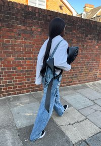 Črna usnjena torba drži na levem roki, v kombinaciji z velikimi svetlo modrimi denim overalli in belo srajco z dolgimi rokavi. Črne športne copate.