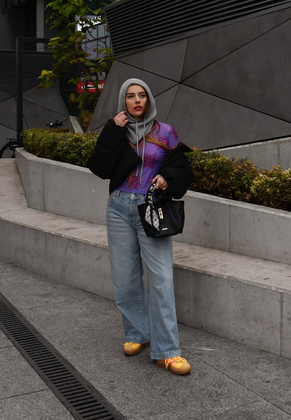 Το μοντέλο φορά ένα μωβ τοπ με λουλουδάτο σχέδιο κάτω από ένα μαύρο oversized σακάκι, ανοιχτού μπλε παντελόνι σε ίσια γραμμή και κίτρινες παντόφλες, κρατώντας μια μαύρη τσάντα.